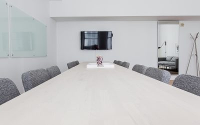 Une salle de réunion moderne avec table blanche, chaises grises et téléviseur mural