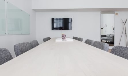 Une salle de réunion moderne avec table blanche, chaises grises et téléviseur mural