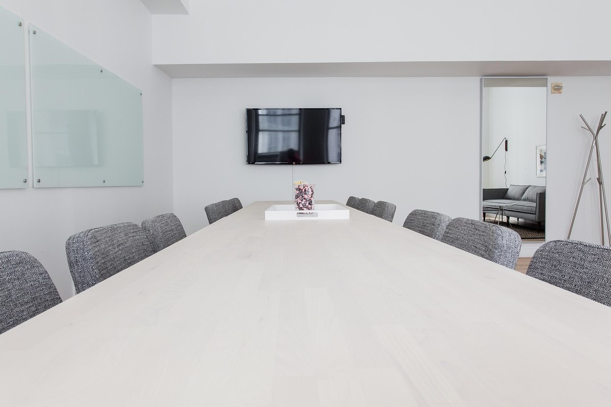 Une salle de réunion moderne avec table blanche, chaises grises et téléviseur mural