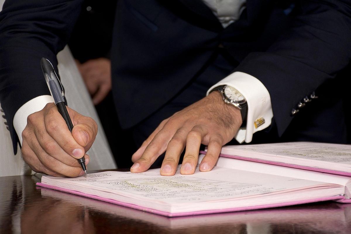 Homme en costume noir signe un document dans un livre à la table Homme en costume noir signe un document dans un livre à la table