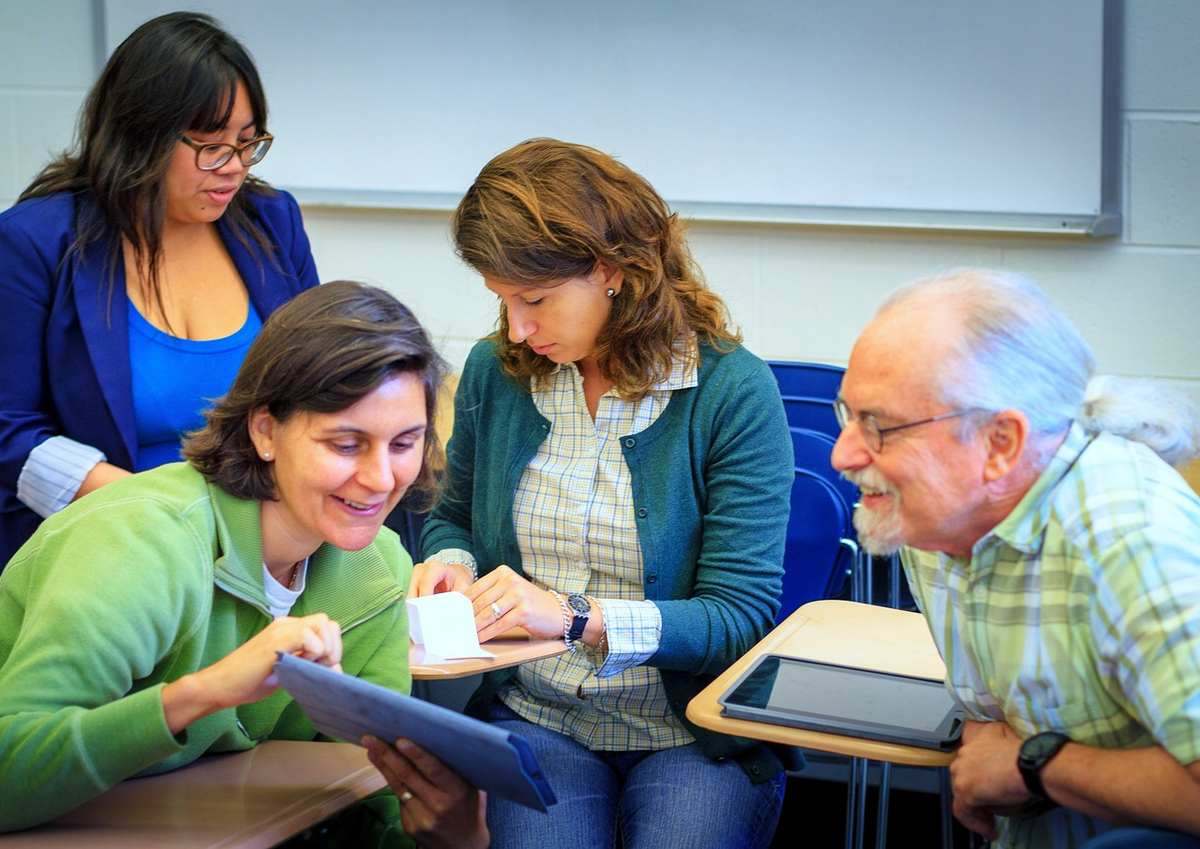 Quatre personnes réunies autour d'une table examinent des documents et une tablette tactile ensemble Quatre personnes réunies autour d'une table examinent des documents et une tablette tactile ensemble