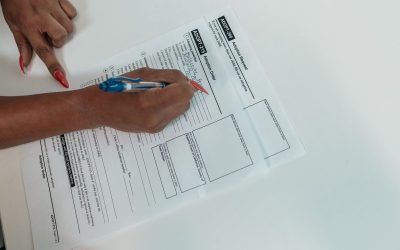 Main gauche pointant vers document, main droite écrivant dessus avec stylo bleu