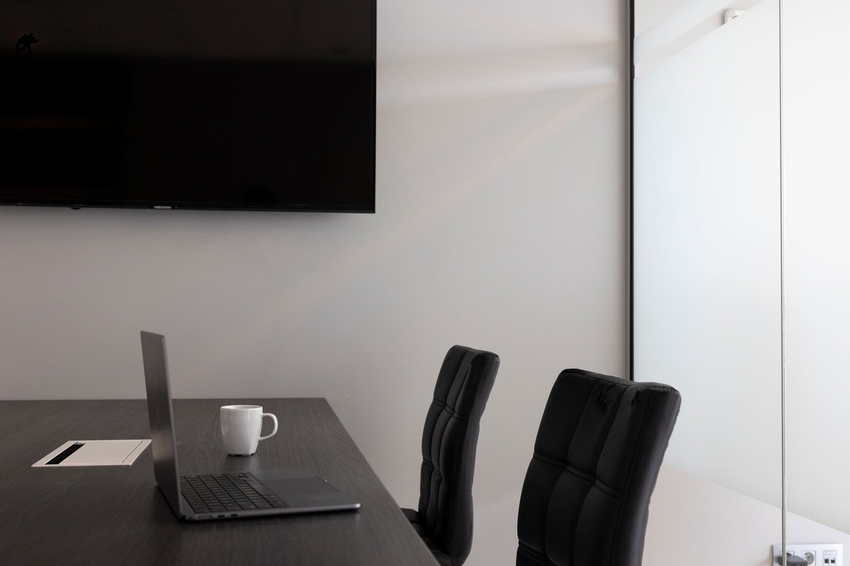 Bureau avec laptop ouvert, tasse blanche, deux chaises noires, écran mural, porte blanche Bureau avec laptop ouvert, tasse blanche, deux chaises noires, écran mural, porte blanche