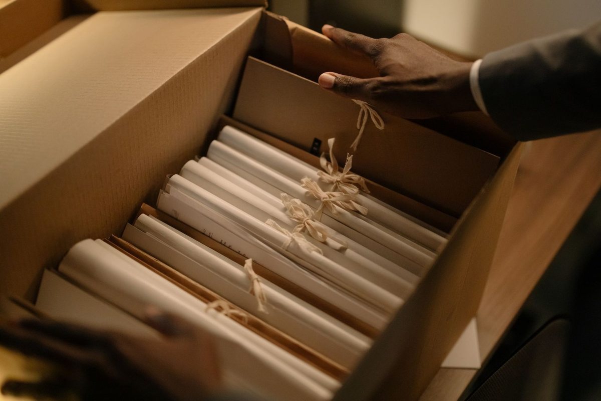 Mains ouvrant un carton avec des documents reliés par ficelle