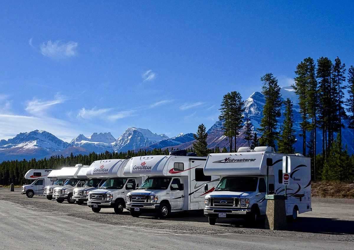Rangée de camping-cars garés côte à côte, chaîne montagneuse enneigée en arrière-plan