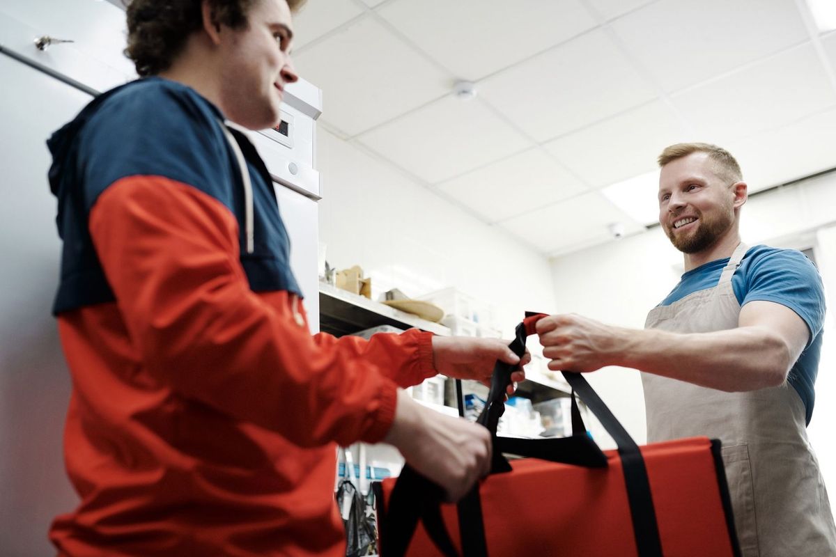 Homme en bleu et homme en orange échangent un sac rouge dans une cuisine Homme en bleu et homme en orange échangent un sac rouge dans une cuisine