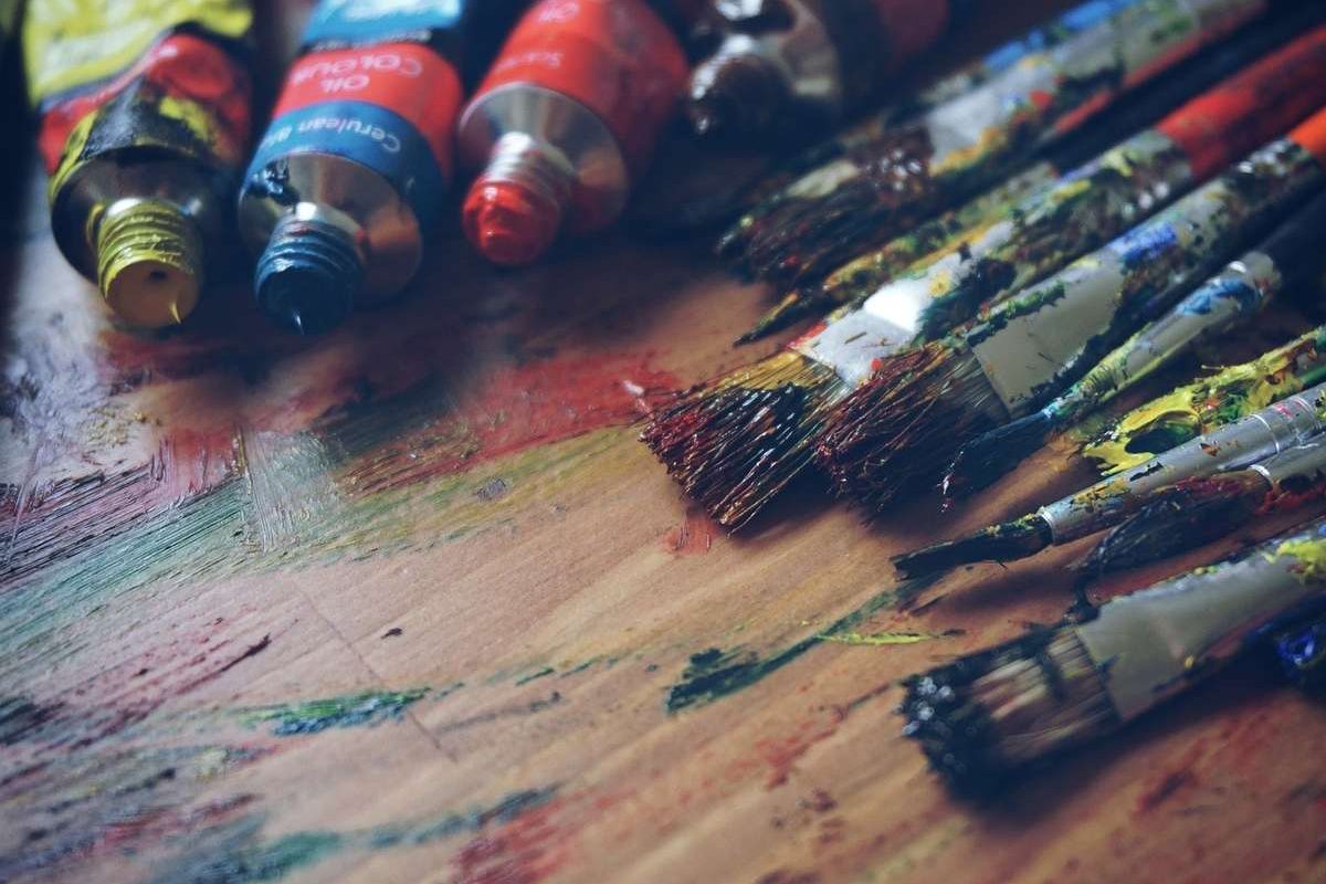 Tubes de peinture et pinceaux sur une table en bois tachée de couleurs