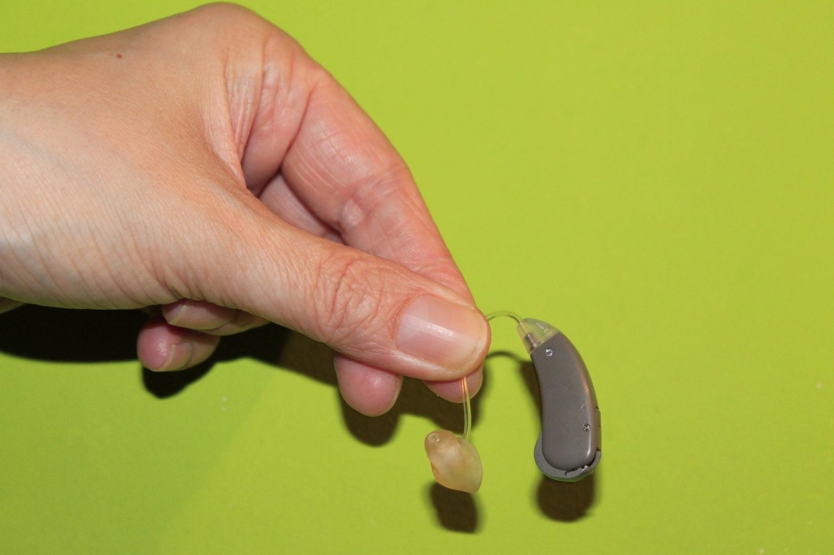 Une main tient un appareil auditif avec embout sur fond vert Une main tient un appareil auditif avec embout sur fond vert