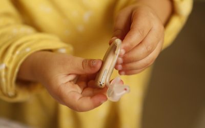 Un enfant en jaune tient un appareil auditif et son petit embout