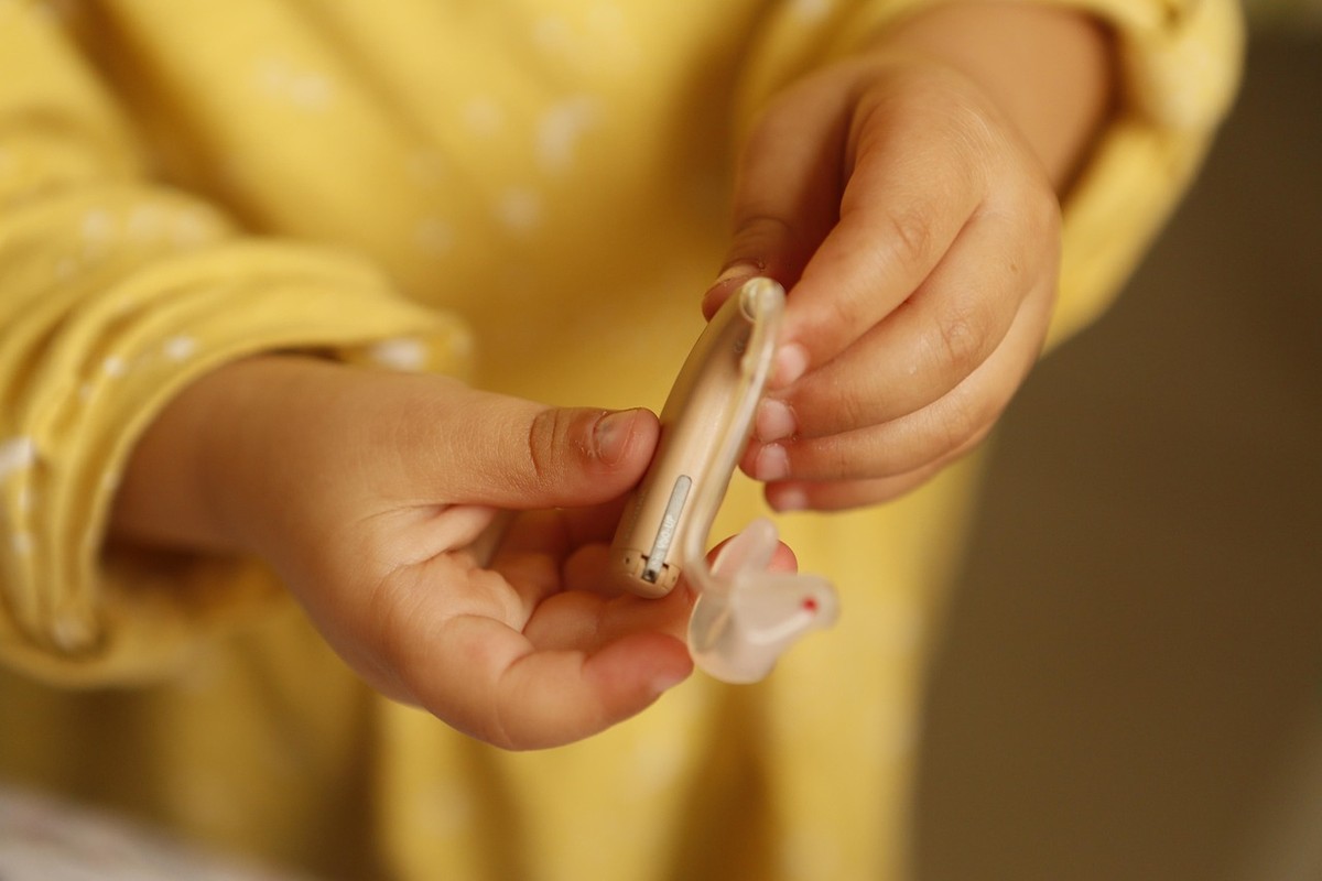 Un enfant en jaune tient un appareil auditif et son petit embout