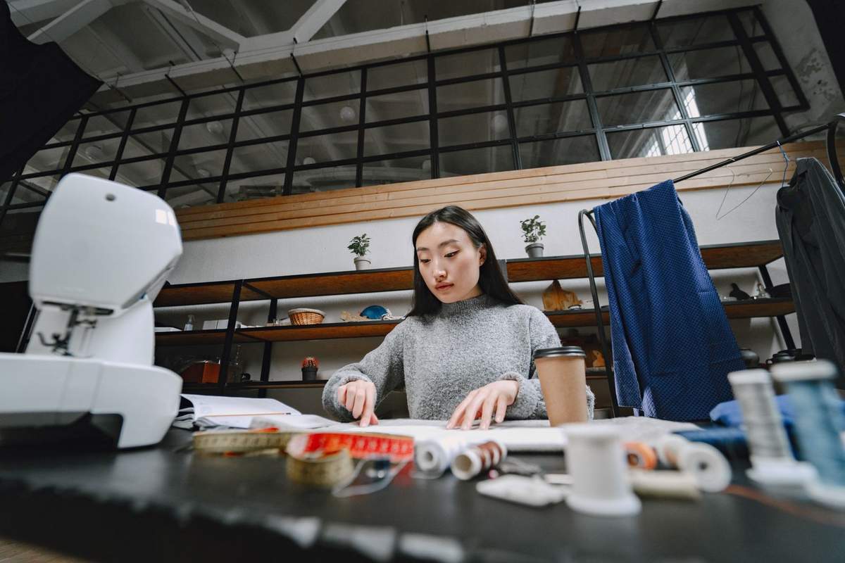 Femme utilisant une machine à coudre avec des fils et du tissu sur une table dans un atelier Femme utilisant une machine à coudre avec des fils et du tissu sur une table dans un atelier