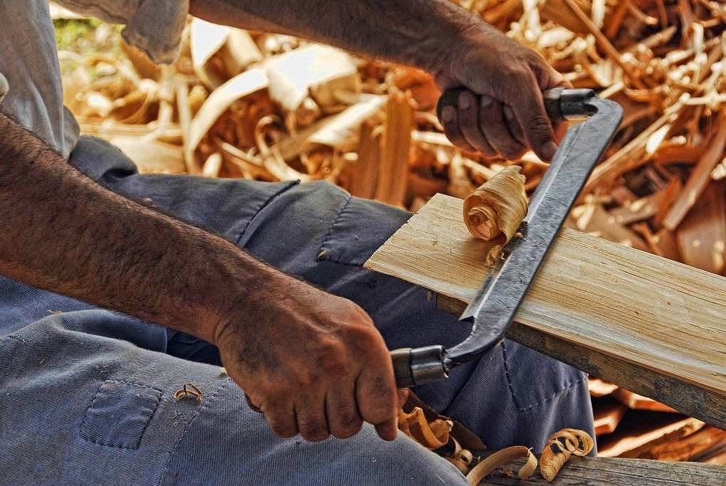 Homme sciant une planche de bois au-dessus de copeaux de bois Homme sciant une planche de bois au-dessus de copeaux de bois