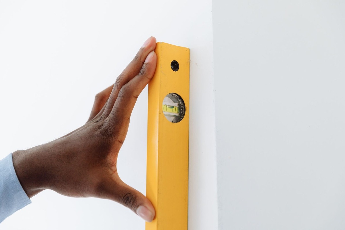 Main noire tenant un niveau à bulle jaune contre un mur blanc Main noire tenant un niveau à bulle jaune contre un mur blanc