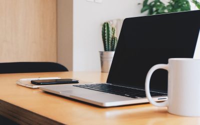 Espace de travail avec ordinateur portable, téléphone, carnet et tasse sur bureau en bois