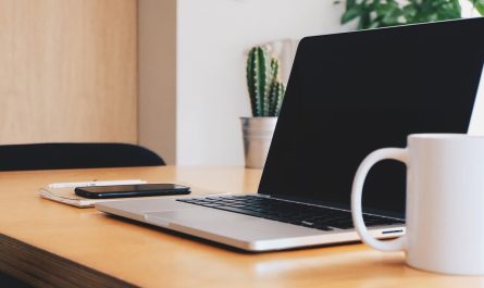 Espace de travail avec ordinateur portable, téléphone, carnet et tasse sur bureau en bois