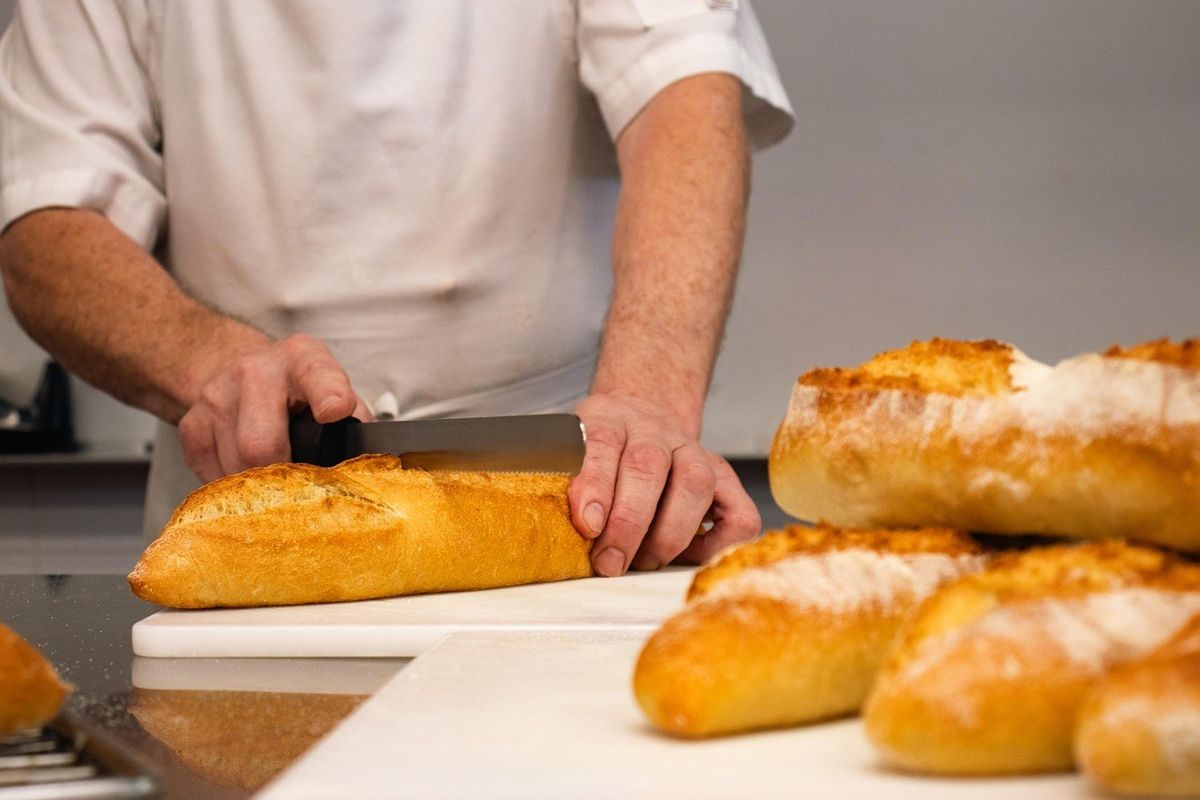 Chef tranchant une baguette sur une planche à découper Chef tranchant une baguette sur une planche à découper