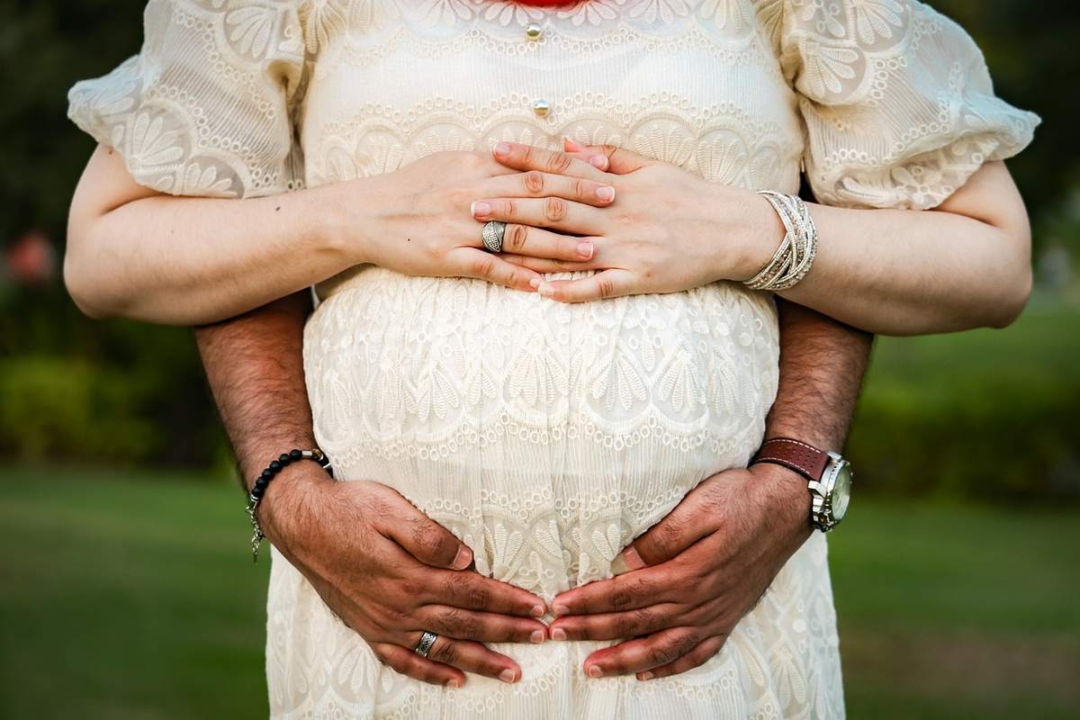 Une femme enceinte en robe blanche un homme soutient son ventre sur gazon Une femme enceinte en robe blanche un homme soutient son ventre sur gazon