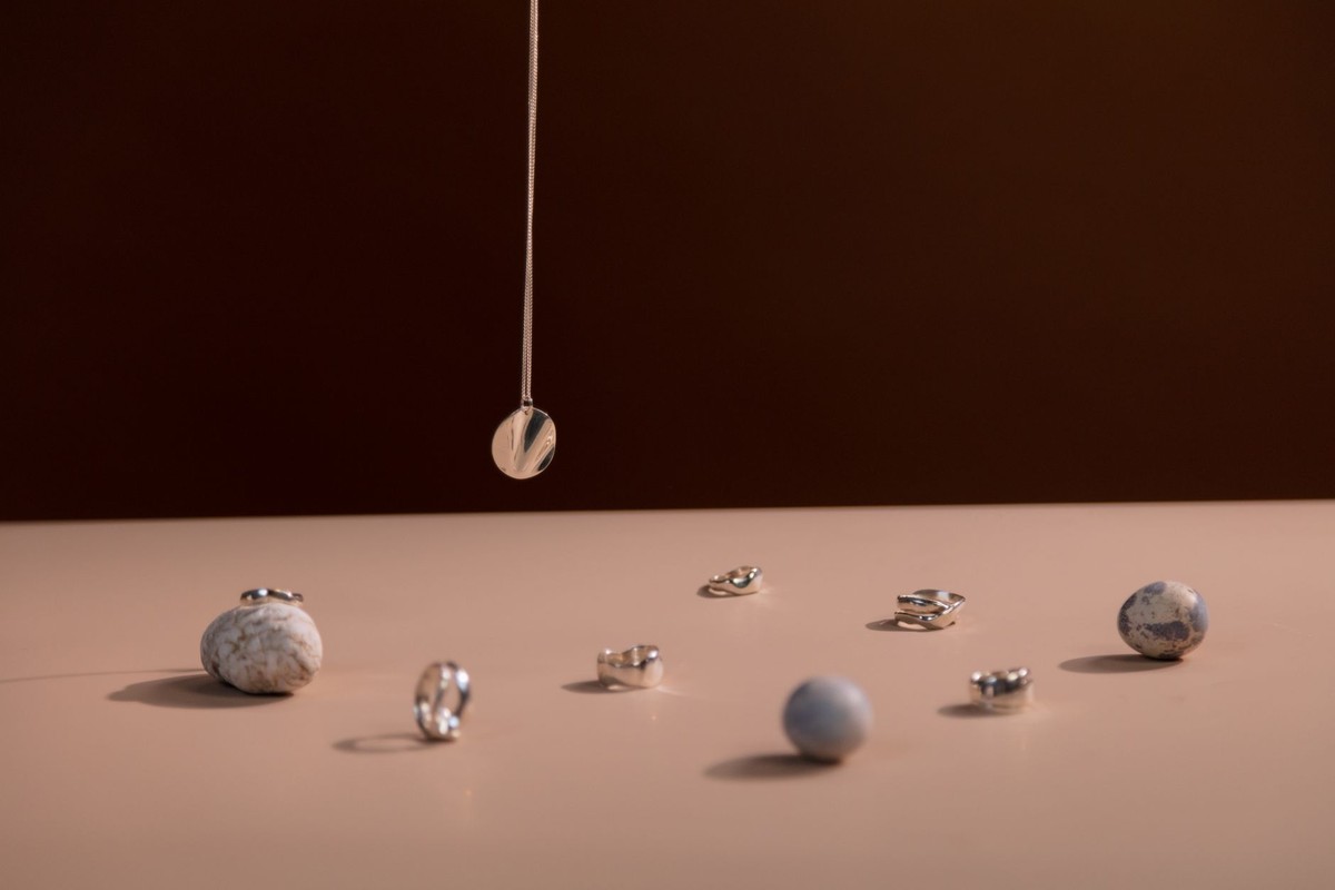 Anneaux et boules métalliques reposent sur une surface claire, un pendentif pend