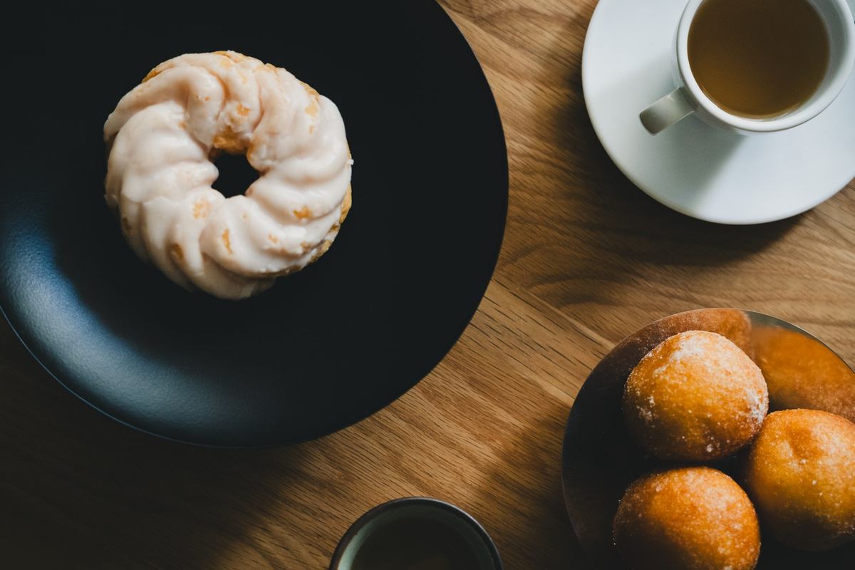 Assiette noire avec beignet, tasse blanche de café, assiette avec trois petits pains sur table en bois Assiette noire avec beignet, tasse blanche de café, assiette avec trois petits pains sur table en bois